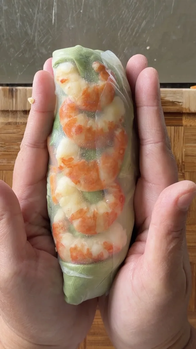 A finished spring roll held up to show the shrimp through the wrapper