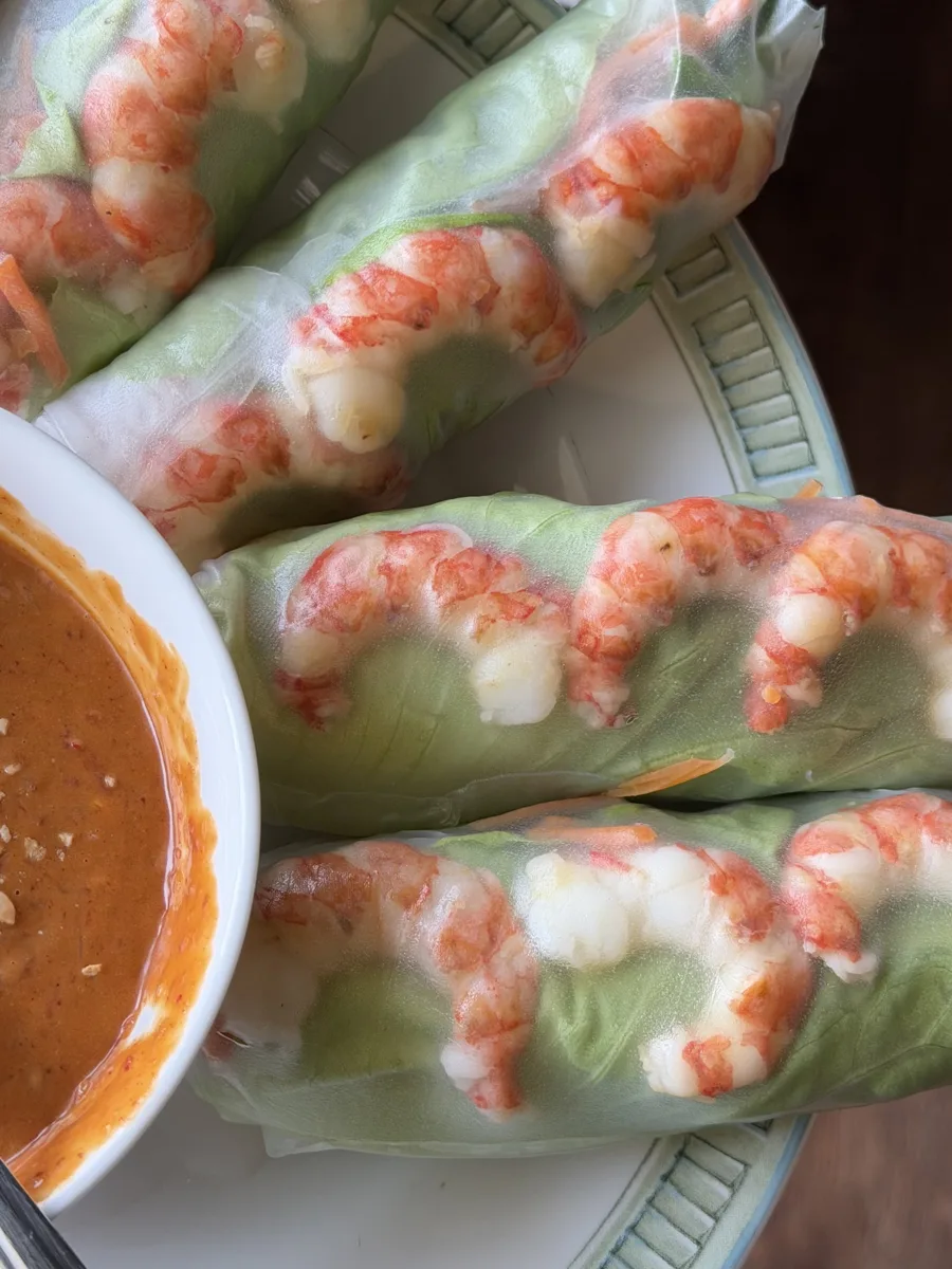 Spot shrimp spring rolls on a plate beside a bowl of peanut-hoisin dipping sauce